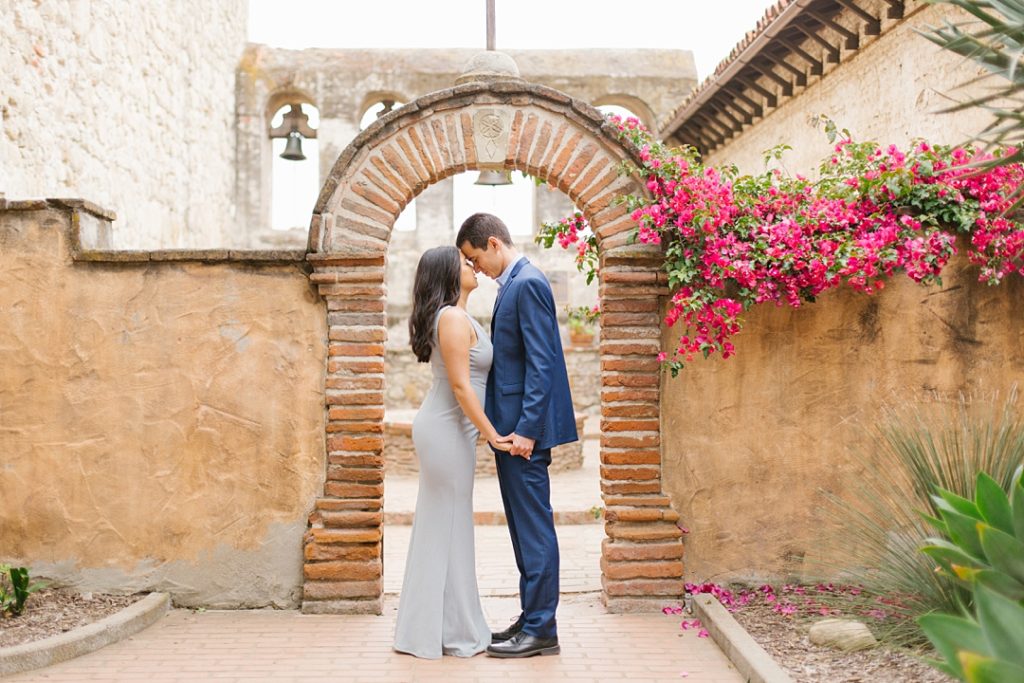 engagement photos in front of arch at Mission San Juan Capistrano