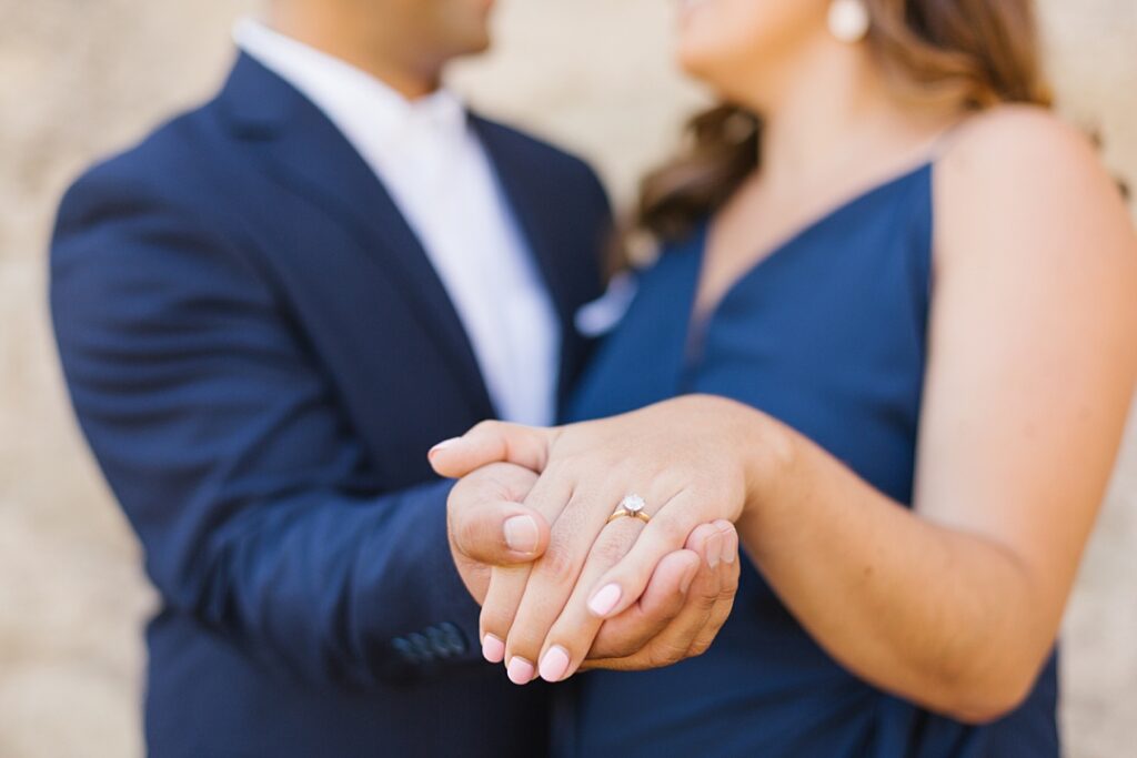 couple in navy blue holds hands for close up photo of engagement ring