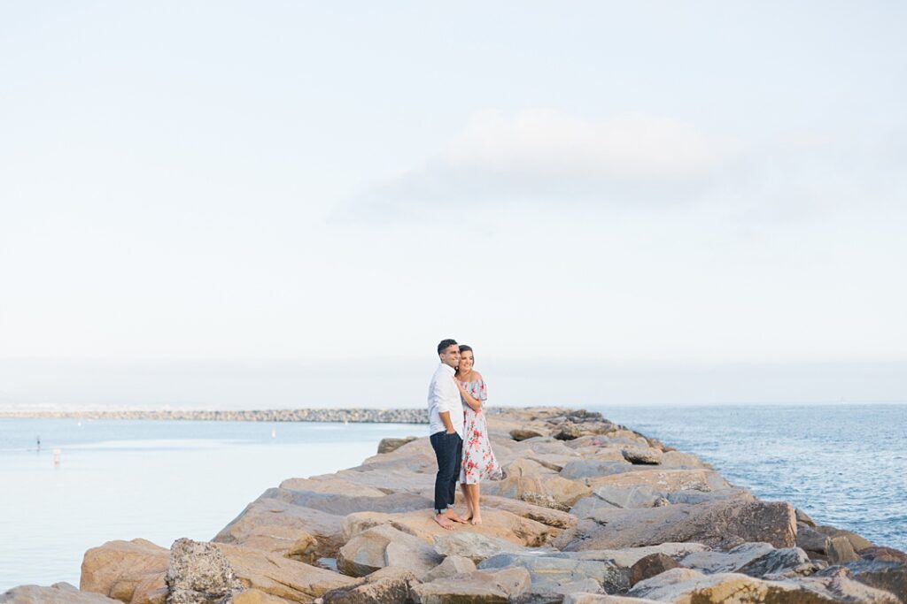 couple stands on rocks at Dana Point Ocean Institute and watches sunset