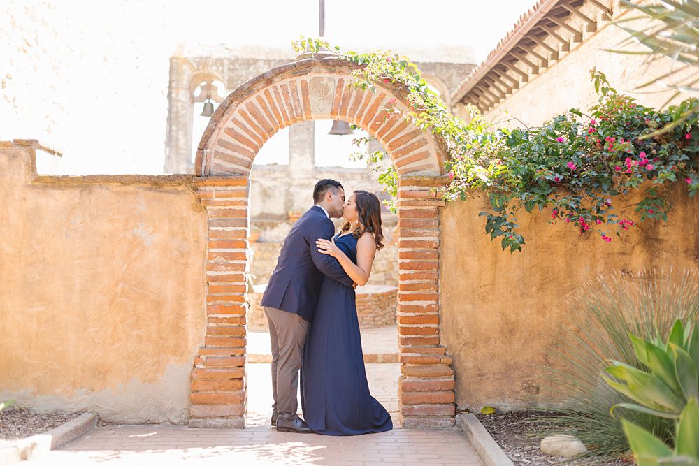 couple kisses under arch at Mission San Juan Capistrano