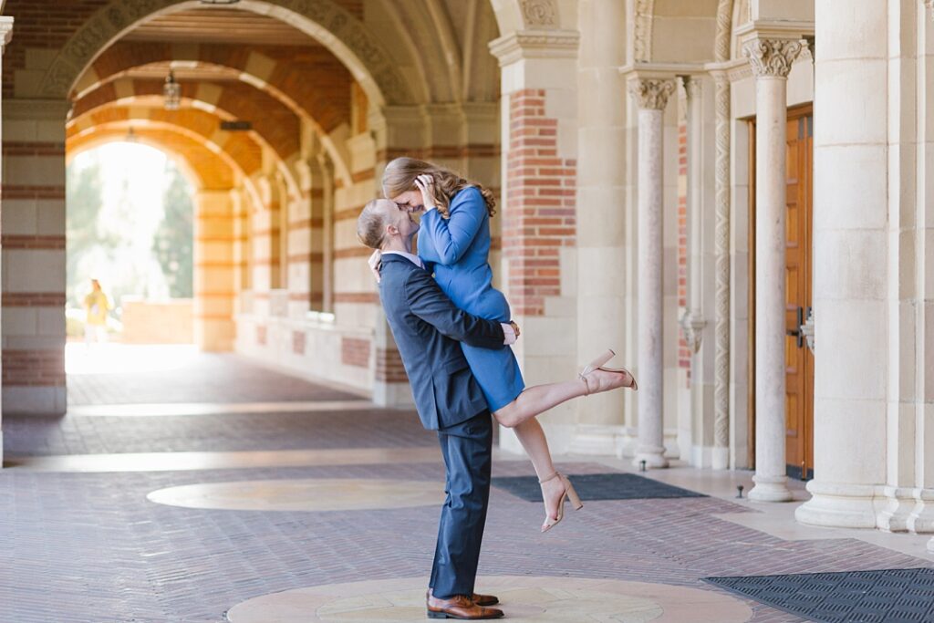 guy lifts up his fiancé at Royce Hall during couples portraits