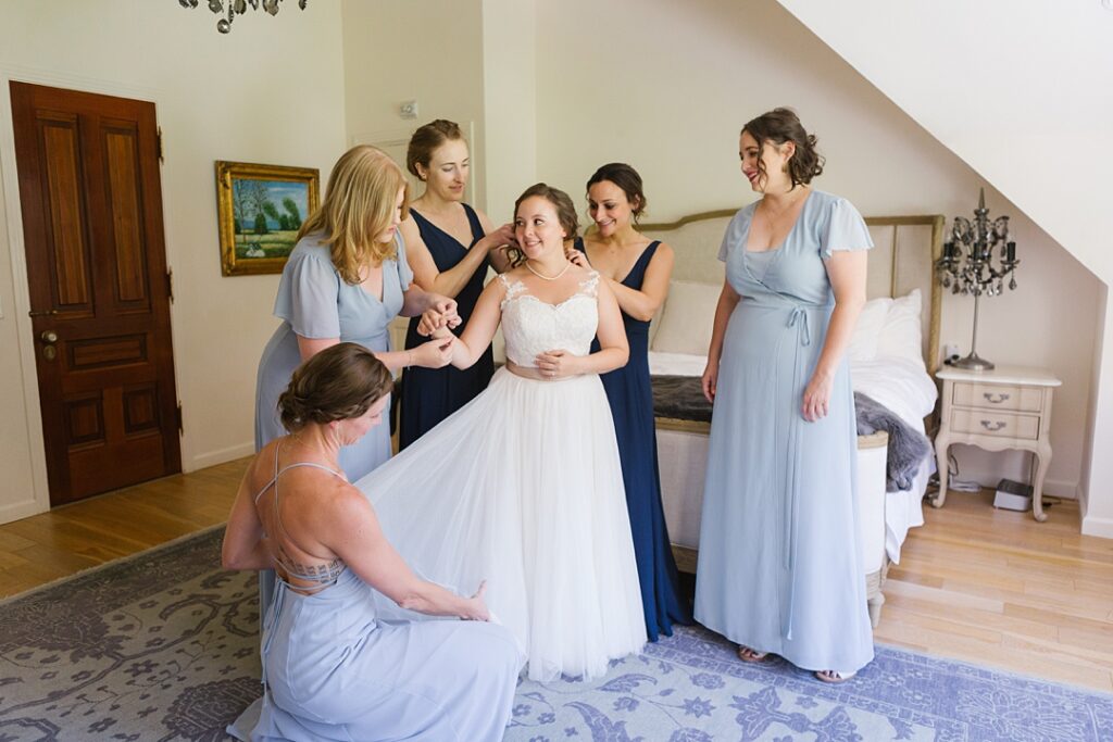 bride gets dressed with help of bridesmaids in blue