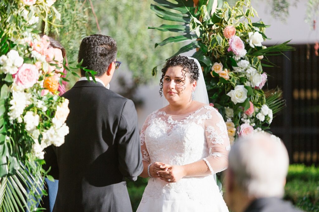 bride in lace sleeved dress stands under chuppah for vows