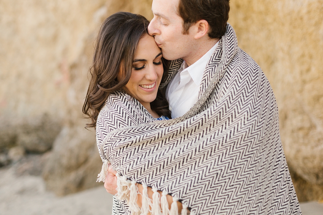 couple snuggles in blanket for beach engagement session
