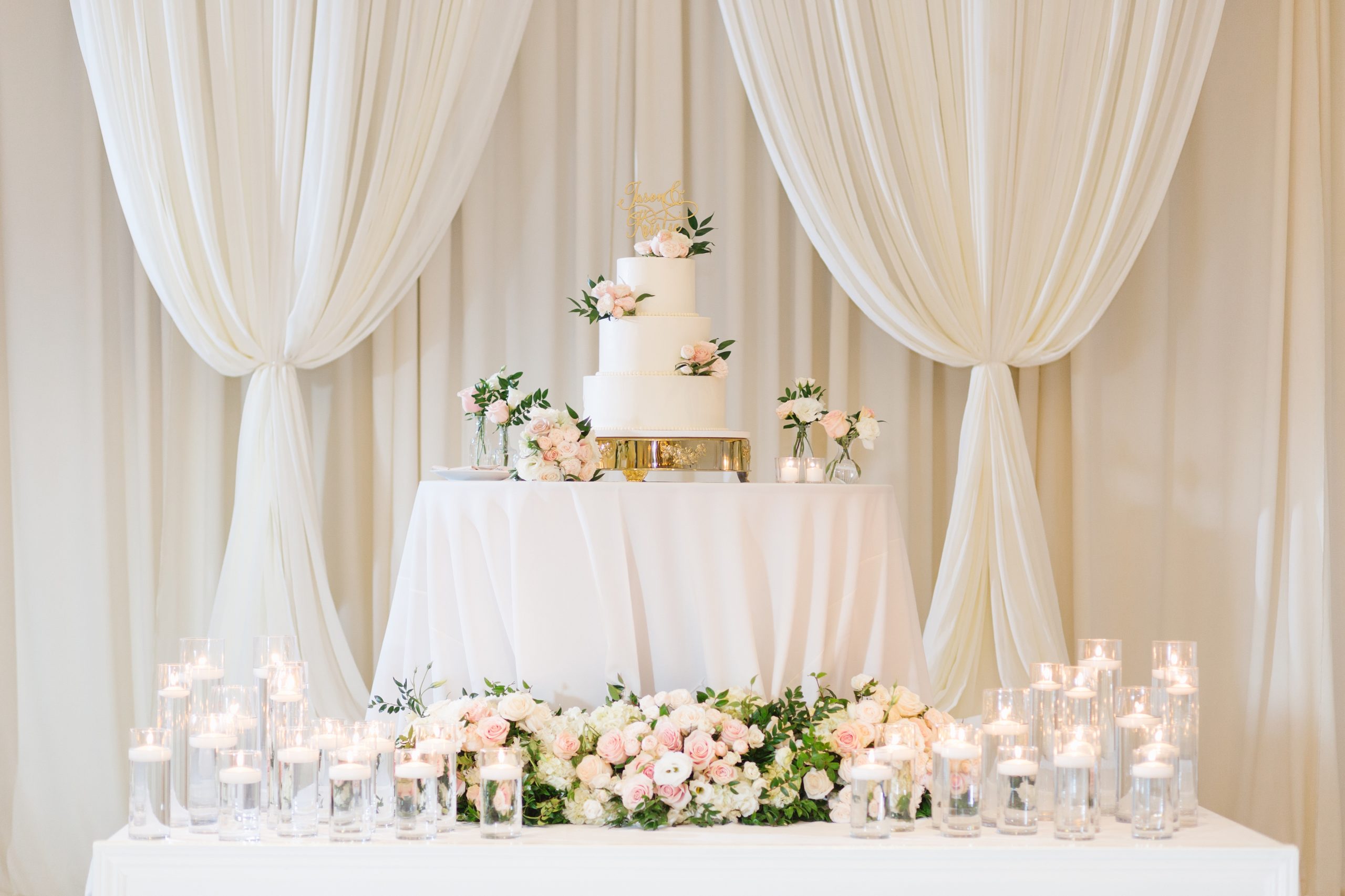 three tier wedding cake surrounded by flowers and candles at luxury Orange County wedding venue