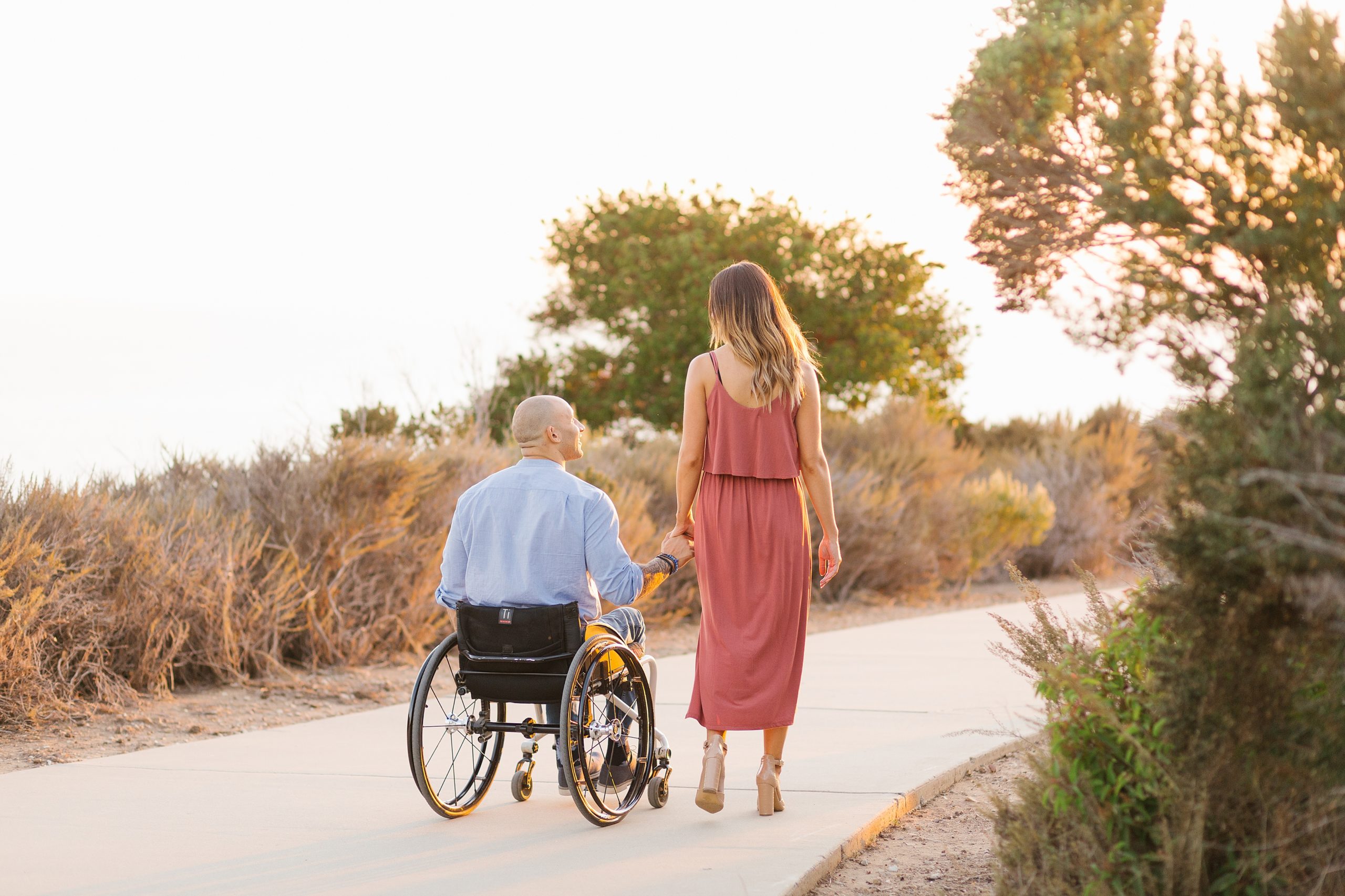 man in wheelchair strolls with woman during sunset engagement session in malibu