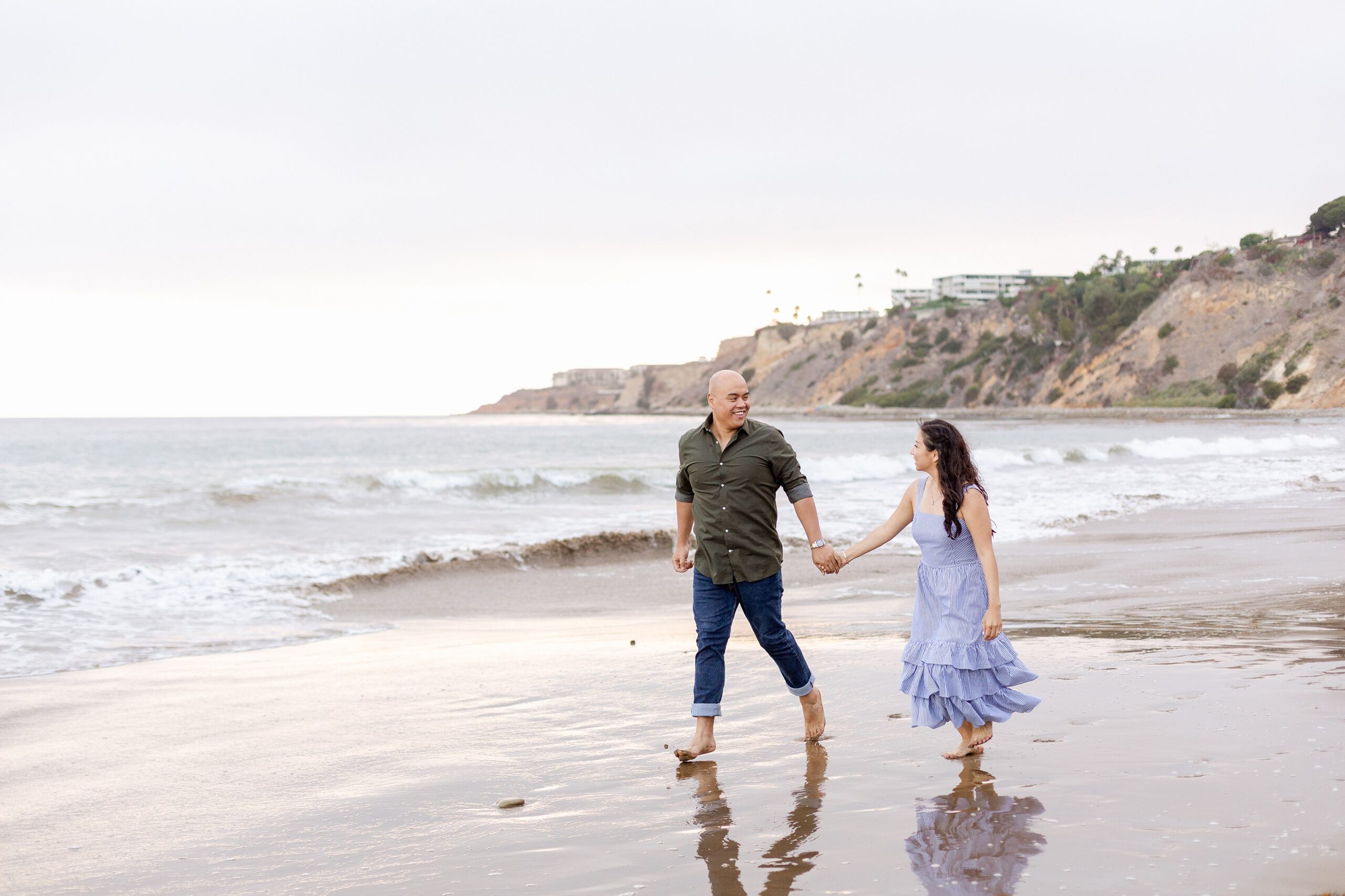 reflection shows in wet sand as couple strolls Abalone Cove for their engagement photos