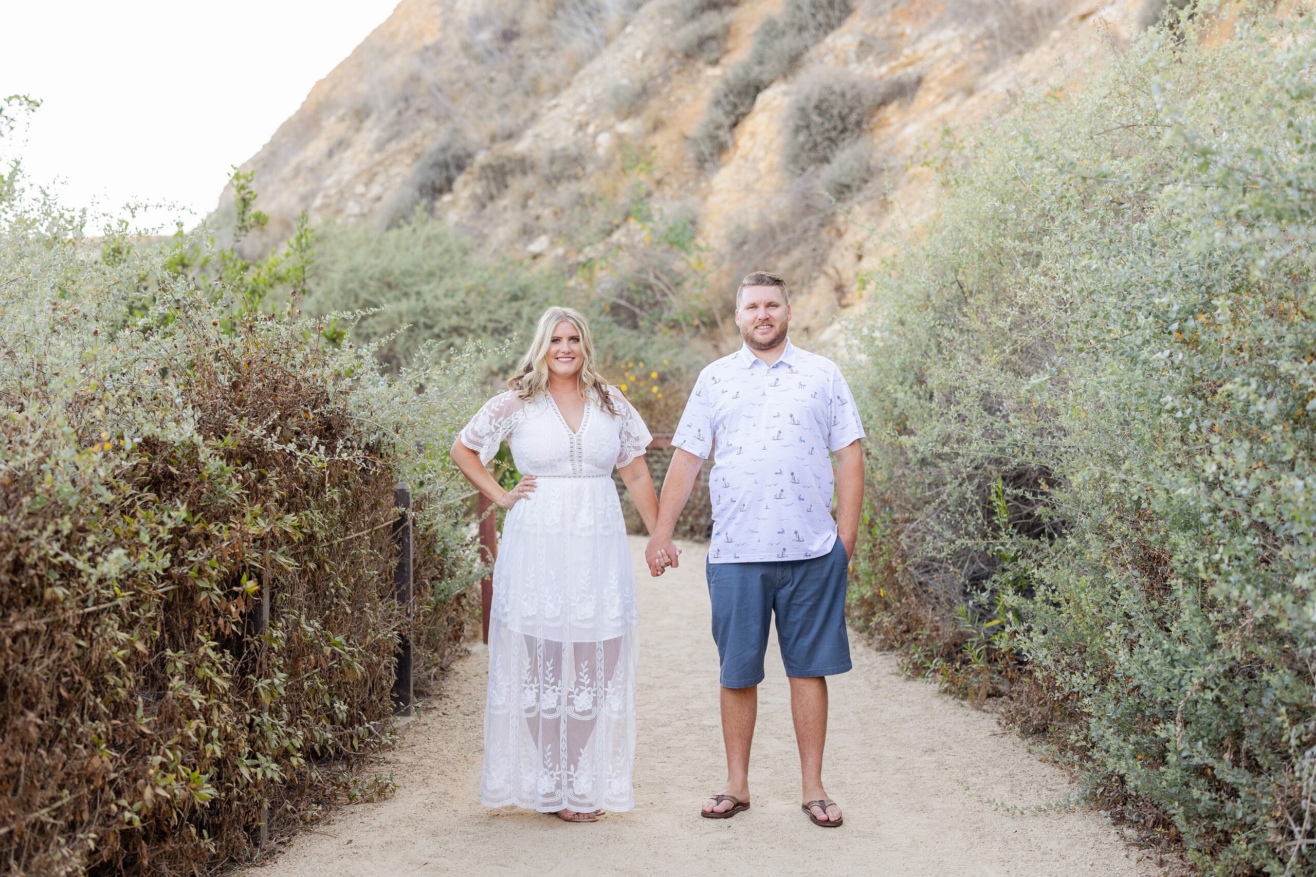 couple holds hands on nature trail leading to beach