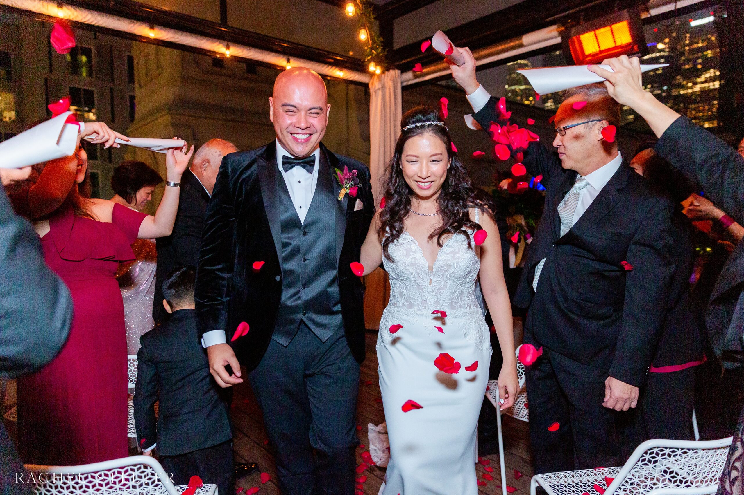 guests throw red rose petals at bride and groom