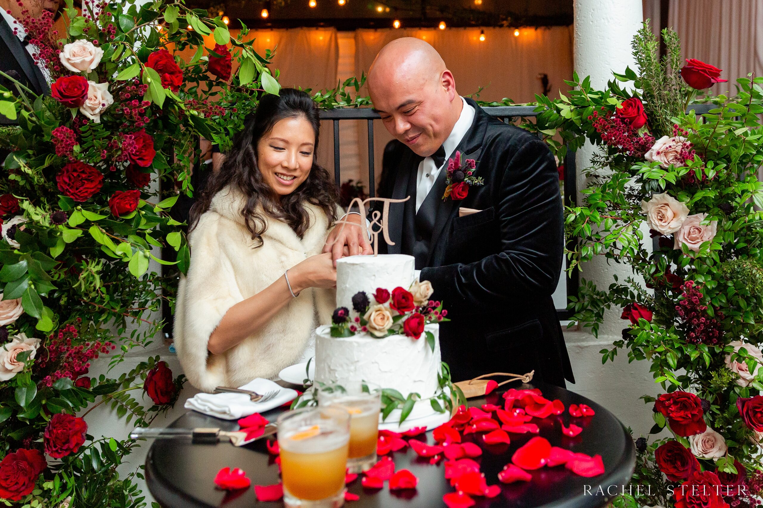 bride and groom are surrounded by red florals as they cut their cake at their downtown los angeles wedding 