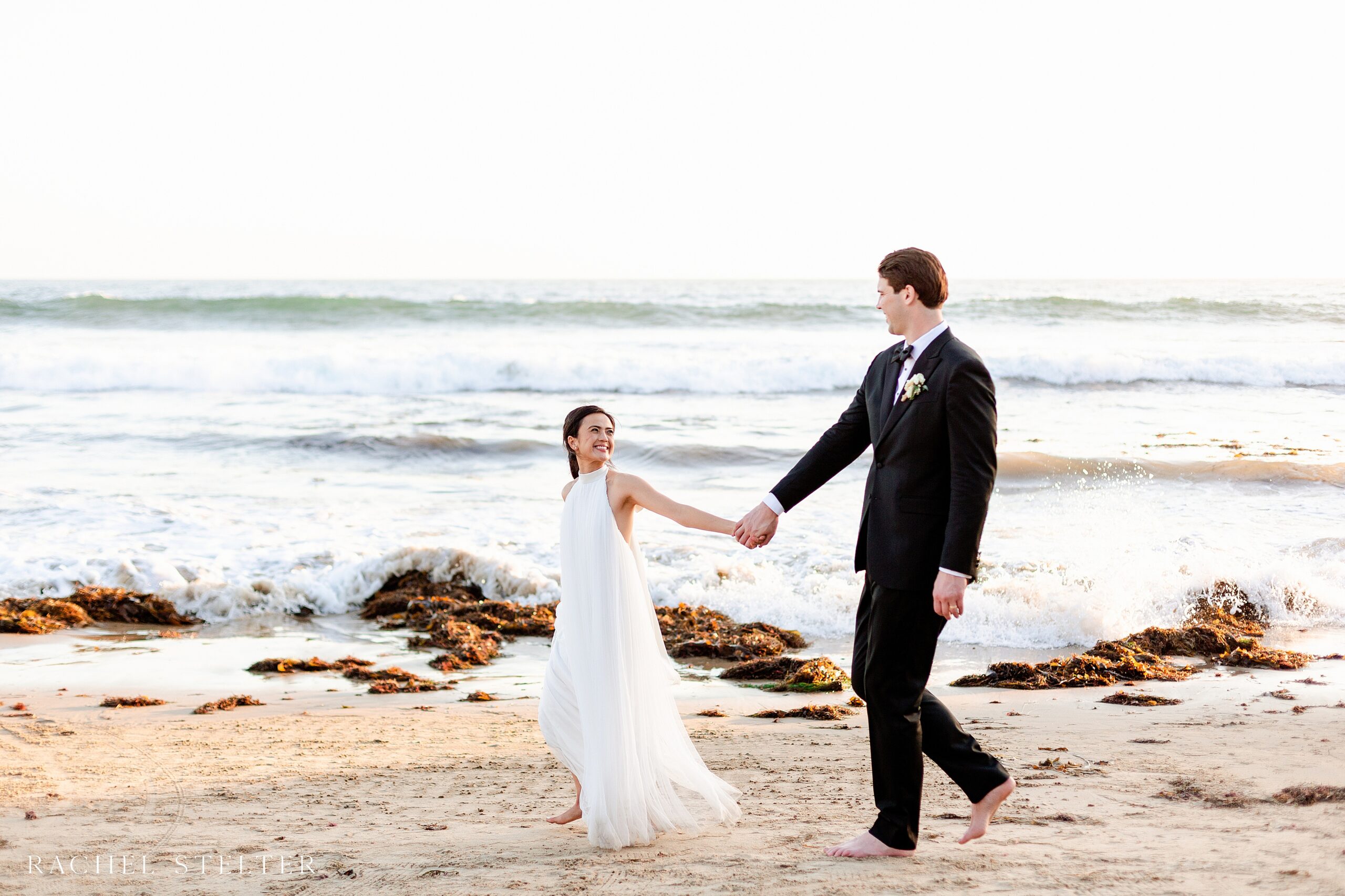 bride and groom walk along beach in Laguna Beach, CA